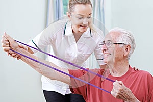 Physiotherapist Helping Senior Male To Use Resistance Band