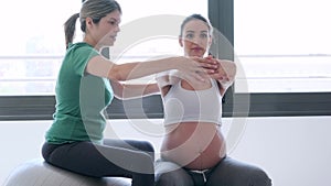 Physiotherapist helping to beautiful pregnant woman for doing pilates exercises with ball preparing for childbirth.
