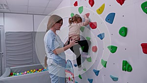 physiotherapist instructor helping little girl to climb wall in gym. sensory integration