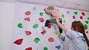 physiotherapist instructor helping little girl to climb wall in gym. sensory integration