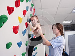 physiotherapist instructor helping little girl to climb wall in gym. sensory integration for kid and correctional