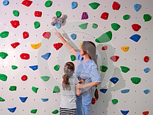 physiotherapist instructor helping little girl to climb wall in gym. sensory integration for kid and correctional