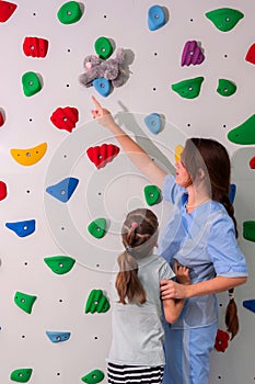 physiotherapist instructor helping little girl to climb wall in gym. sensory integration for kid and correctional