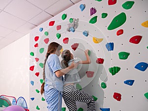 physiotherapist instructor helping little girl to climb wall in gym. sensory integration for kid and correctional