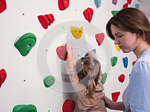 physiotherapist instructor helping little girl to climb wall in gym. sensory integration for kid and correctional