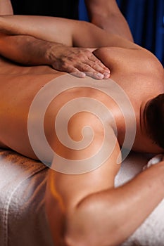 Physiotherapist massaging male patient with damaged scapula muscle, treating sports injuries. Relaxing professional