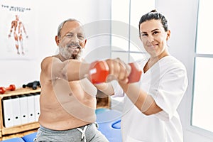 Physiotherapist and patient smiling confident having rehab session using dumbbell at clinic