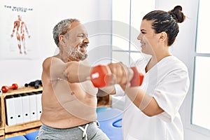 Physiotherapist and patient smiling confident having rehab session using dumbbell at clinic