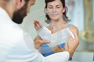 Physiotherapist putting bandage on injured hand of patient photo