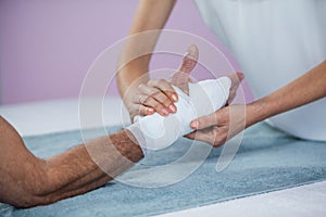 Physiotherapist putting bandage on injured hand of patient