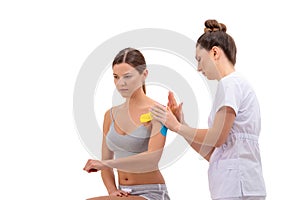 Physiotherapist putting on kinesio tape on female patients shoulder isolated on white background