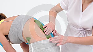 Physiotherapist sticks kinesio tapes to the small of the back of female patient, kinesiology taping, kinesiological