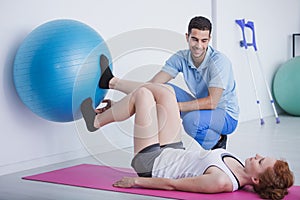 Physiotherapist supporting woman exercising with rehabilitation ball