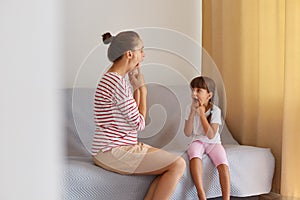 Physiotherapist wearing striped casual shirt working on speech defects or difficulties with small child girl at home while sitting