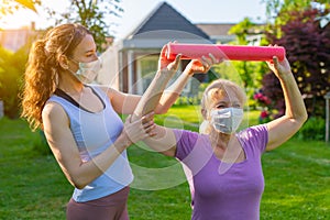 Physiotherapist working with elderly patient outdoors both wearing medical masks