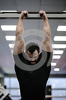 Physique development of young bearded male in black jersey holding crossbar for stretching during gym sport workout