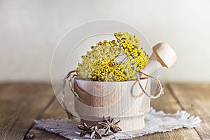 Phytotherapy, collecting medicinal herbs for tea and mixtures. Dried tansy flowers in a wooden mortar with pestle on a rustic