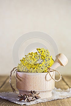 Phytotherapy, collecting medicinal useful herbs. Dried tansy flowers in a wooden mortar with pestle on a rustic background