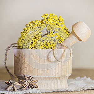 Phytotherapy, collecting medicinal useful herbs. Dried tansy flowers in a wooden mortar with pestle on a rustic background