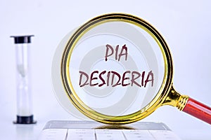 PIA DESIDERIAPIA the phrase in Latin means Good intentions through a magnifying glass on a gray background next to an hourglass photo