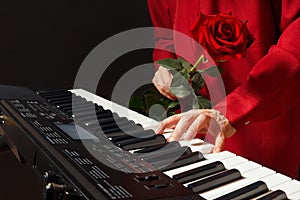 Pianist with red rose playing the electronic piano on black background