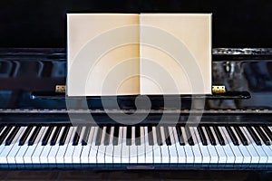 Piano keyboard with musical notebook in concert.Blank paper sheet on black grand piano.