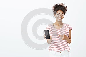 Pick this phone model. Portrait of satisfied happy african-american woman in glasses and striped t-shirt, showing