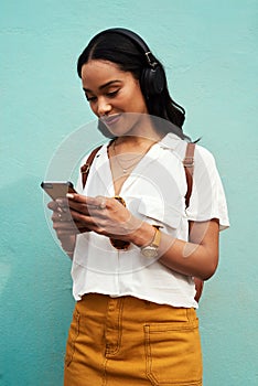 Picking out the best song for the city. an attractive young woman standing alone and listening to music while texting