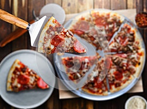 Picking up slice of meaty sausage and pepperoni pizza top down view