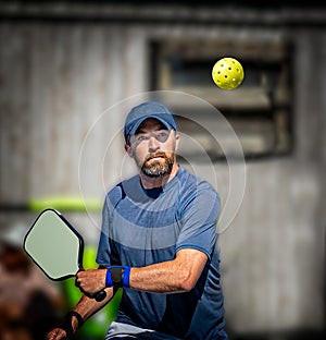 Pickleball player about to hit the yellow plastic ball with his paddle