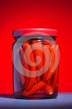 Pickled chili pepper in a glass jar on a red background