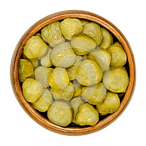 Pickled cucumber discs, known as pickle or gherkin, in wooden bowl