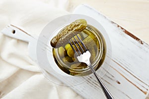 Pickled cucumbers on a fork and in a jar on a wooden background.