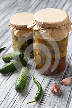 Pickled cucumbers in glass jars and spices and vegetables for preparation of pickles on old wooden background