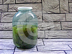 Pickled cucumbers in jar on stone background