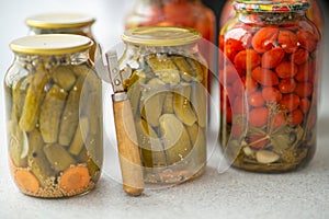 Pickled cucumbers and tomatoes in glass jar on a white background with opener