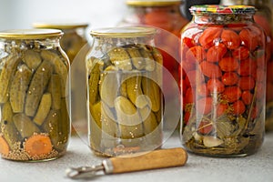 Pickled cucumbers and tomatoes in glass jar on a white background with opener