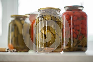 Pickled cucumbers and tomatoes in glass jar on a white background with opener