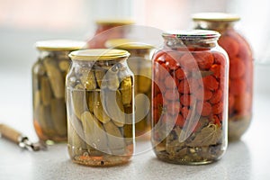 Pickled cucumbers and tomatoes in glass jar on a white background with opener