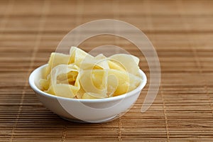 Pickled ginger slices in white ceramic bowl on bamboo mat.