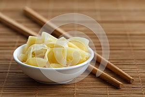 Pickled ginger slices in white ceramic bowl on bamboo mat next t