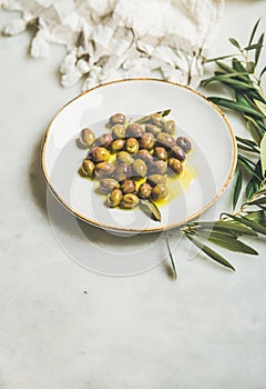 Pickled green Mediterranean olives in olive oil on white plate