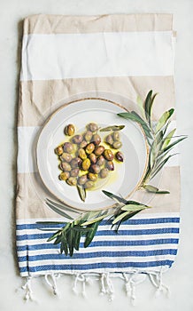 Pickled green Mediterranean olives on white ceramic plate, top view