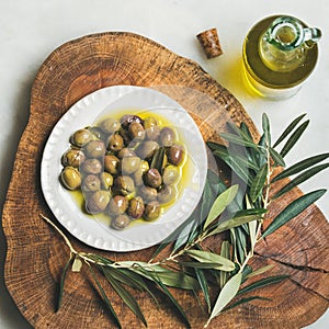 Pickled green Medoterranean olives and olive-tree branch on wooden board