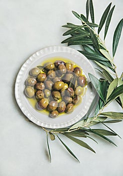 Pickled green olives and olive-tree branch over marble background