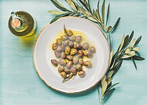 Pickled green olives, olive tree branch, virgin oil, blue background