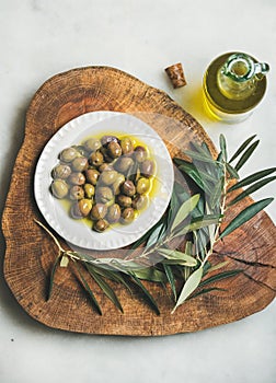 Pickled green olives and olive-tree branch on wooden board
