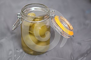 Pickled green small tomatoes in a glass jar with a lid on a gray background. Salted cherries, home-made,