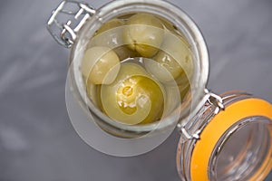 Pickled green small tomatoes in a glass jar with a lid on a gray background. Salted cherries, home-made,