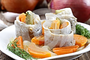 Pickled herring rolls with vegetables on wooden table